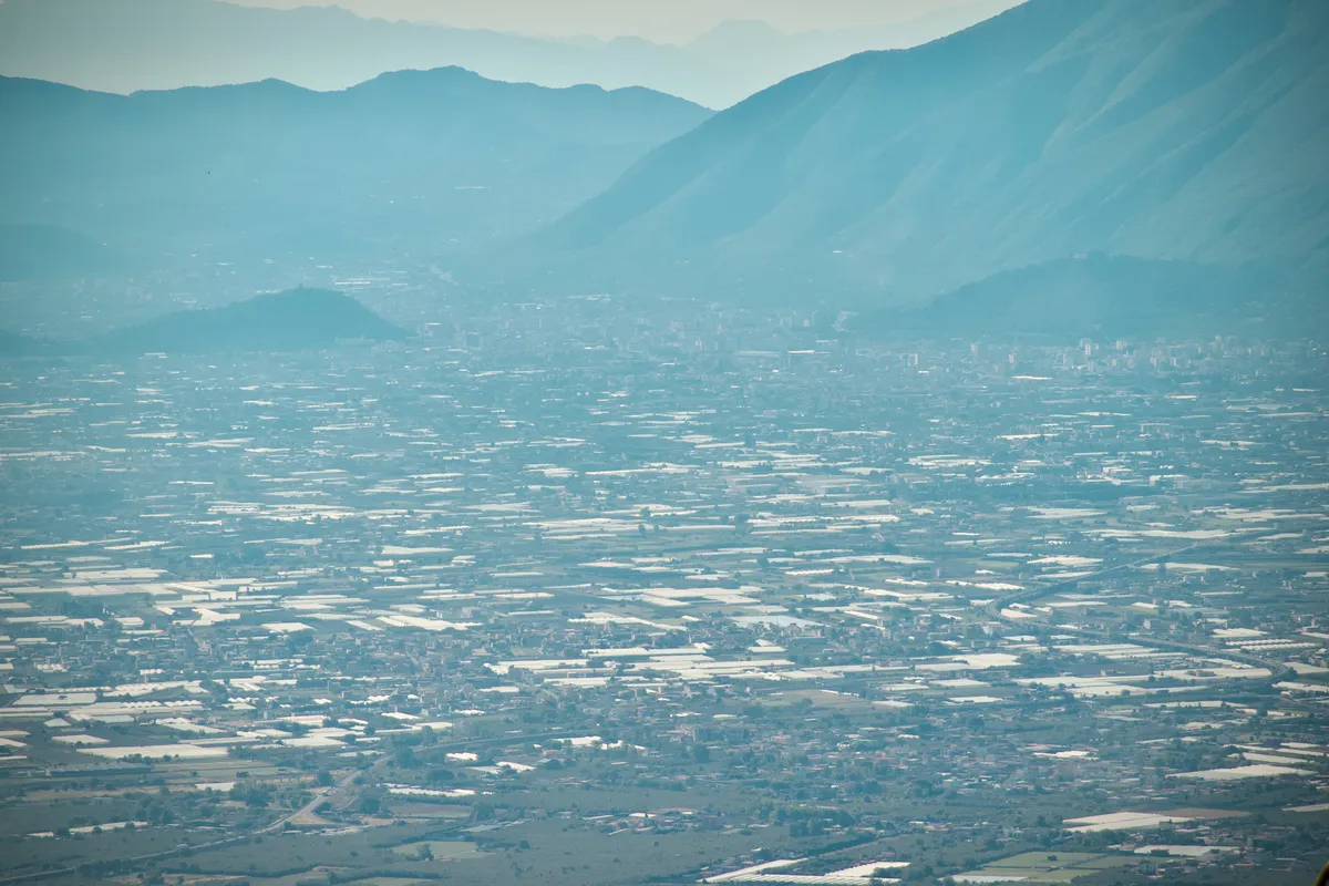 Aerial view of vast plains and agricultural fields stretching toward layered mountain ranges in hazy atmospheric perspective, taken from Mount Vesuvius, Italy