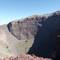 Deep volcanic crater of Mount Vesuvius showing steep rocky walls with visible geological layers and sparse green vegetation on crater floor, Naples, Italy