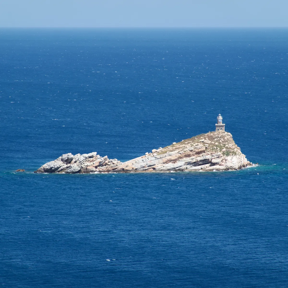 White lighthouse perched on top of layered rocky sea stack surrounded by deep blue Mediterranean waters near Portoferraio, Italy