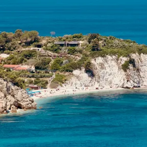 Small secluded beach with white sand nestled between tall limestone cliffs, showing beachgoers and clear blue water at Padulella Beach, Portoferraio, Italy
