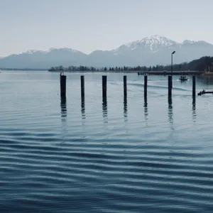 Seven wooden posts standing in calm lake water with snow-capped Bavarian Alps in background at Chiemsee, Germany