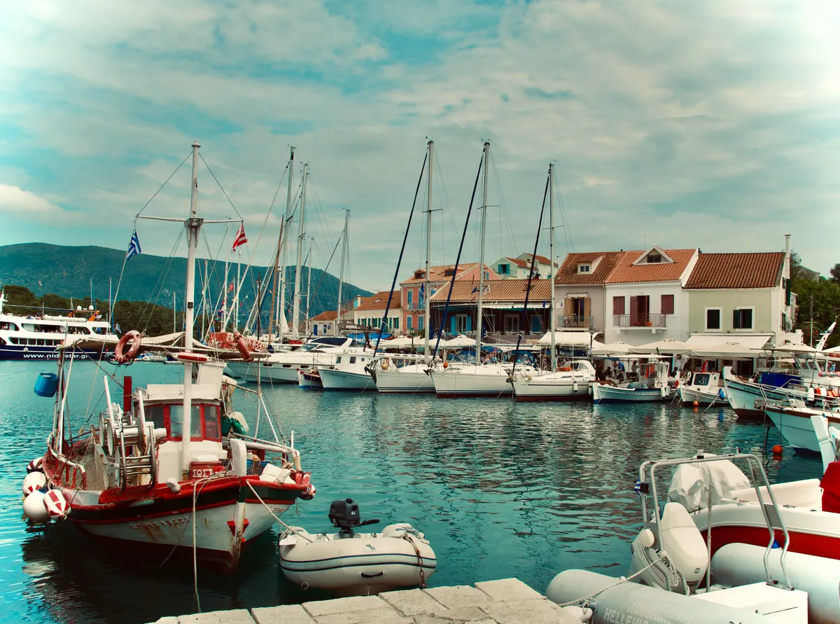 Harbor view of Fiskardo, Greece showing various boats moored in turquoise water with traditional white buildings and red tile roofs along waterfront