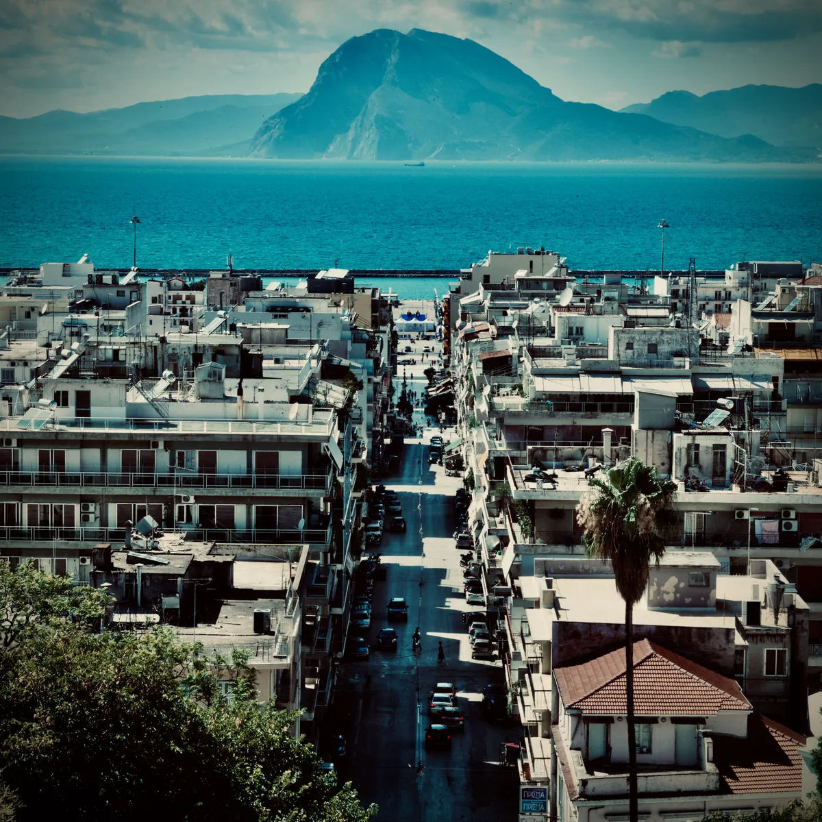 Aerial view of Patras, Greece showing white buildings, main street leading to harbor, mountains across Ionian Sea in background