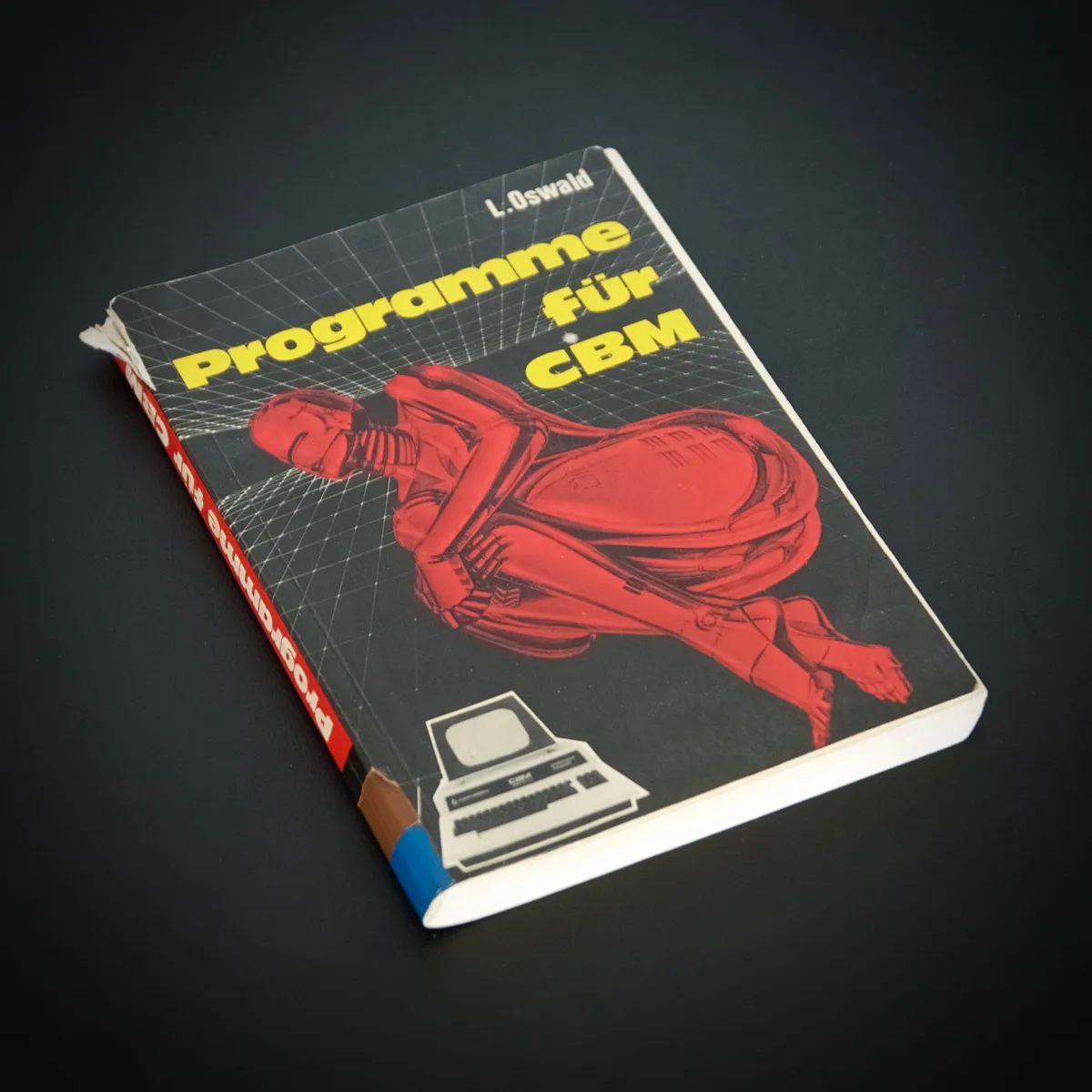 Vintage 1981 programming book 'Programme für CBM' by L. Oswald with black cover featuring red robot illustration and grid pattern background