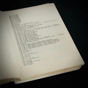 Open programming book showing multiple pages of BASIC code listings with line numbers, PRINT statements, and GOSUB commands in monospace font