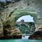 View through natural stone arch showing medieval tower on cliff overlooking turquoise Adriatic Sea in Vieste, Italy
