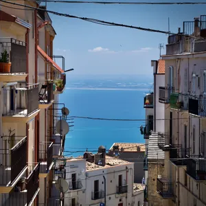 Narrow street in Monte Sant'Angelo, Italy with colorful buildings, balconies, and view of blue Adriatic Sea in background