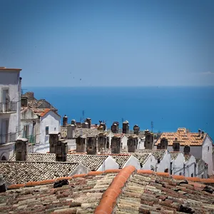 View from rooftop in Monte Sant'Angelo showing terracotta tile roofs, multiple chimneys, white buildings and blue sea horizon