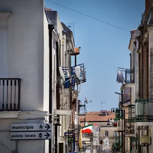 Italian street signs directing to municipality and local police, narrow street with white buildings, balconies, and Italian flag