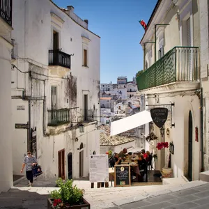 Outdoor restaurant terrace in Monte Sant'Angelo, Italy with diners at tables, white stone buildings, balconies, and hillside town view