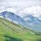 Rolling green hills leading to dramatic limestone mountain peaks under cloudy sky in L'Aquila, Abruzzo, Italy