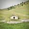 Small stone cottage with circular windows surrounded by dry stone walls in green rolling hills near Barisciano, Italy