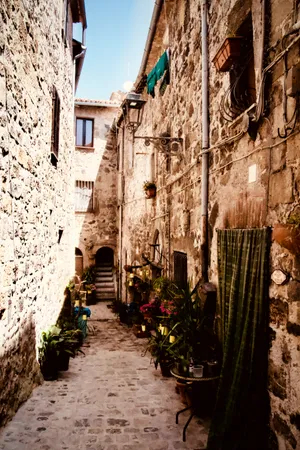 Narrow cobblestone alley in Bolsena, Italy with weathered stone walls, potted plants, laundry hanging, and traditional doorways