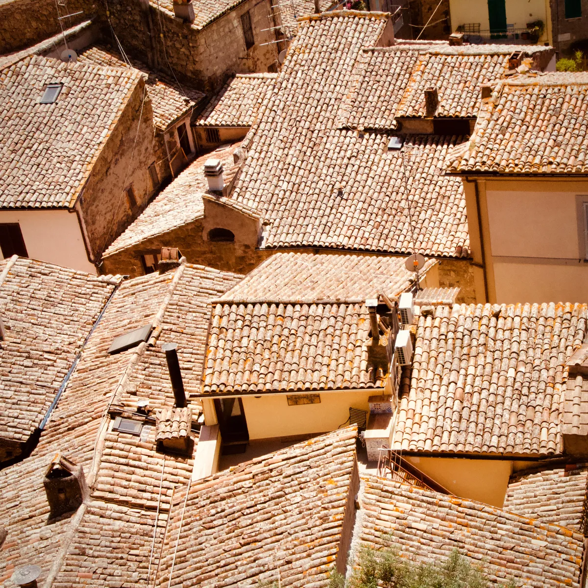 Overhead view of densely packed terracotta tile rooftops with stone chimneys and walls in Bolsena, Italy