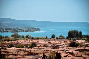 Panoramic view of Bolsena, Italy with terracotta-roofed buildings in foreground overlooking Lake Bolsena and forested hills