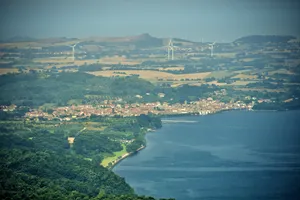 Aerial view of Lake Bolsena, Italy showing a hillside town along the shoreline with wind turbines scattered across rolling agricultural landscape