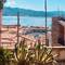 Harbor view of Portoferraio showing colorful buildings, marina with boats, and Mediterranean mountains framed by large agave plants on Elba Island, Italy