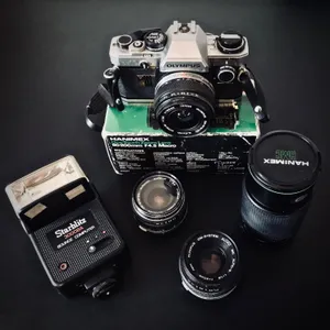 Vintage Olympus OM-10 camera with chrome body, various lenses, flash unit, and lens box arranged on dark surface in Austria