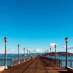 Long wooden pier extending over San Francisco Bay with ornate lampposts, metal railings, and people walking, Telegraph Hill, California