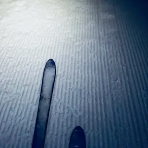 Tips of backcountry skis on groomed snow slope with corduroy texture pattern, taken during uphill ski touring in Austrian Alps
