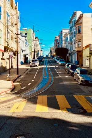 Steep San Francisco street with cable car tracks running uphill between colorful Victorian buildings, yellow crosswalk stripes in foreground