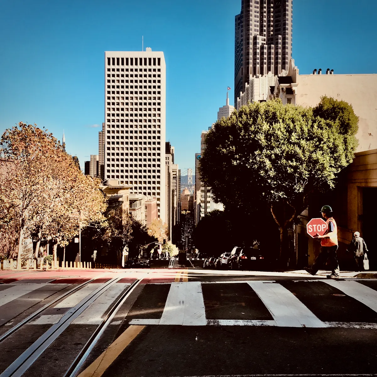 Construction worker in safety vest holding stop sign on San Francisco street with cable car tracks, downtown skyscrapers in background