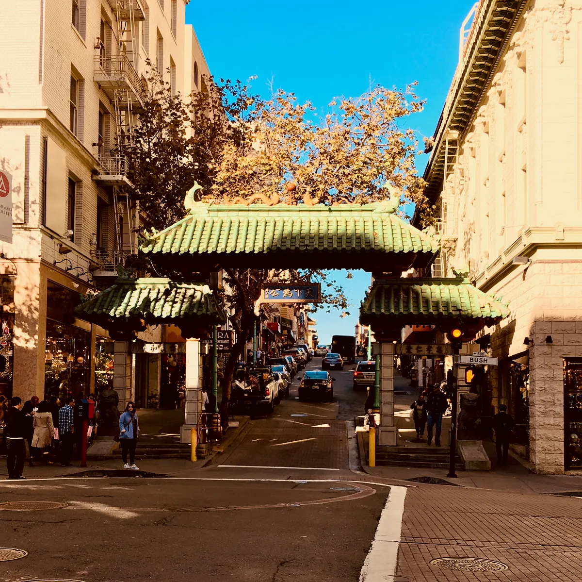 Traditional Chinese pagoda gate with green tile roof spanning street intersection in San Francisco Chinatown, with people walking below