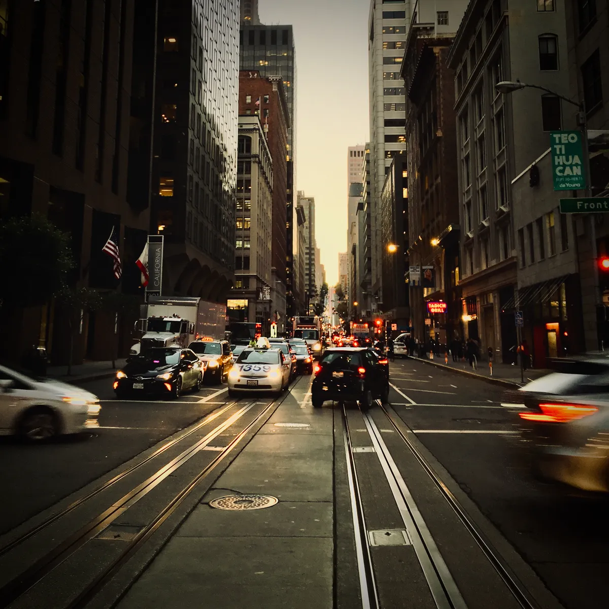 Cable car tracks running down busy San Francisco street with traffic, tall buildings on both sides, evening lighting in SoMa district