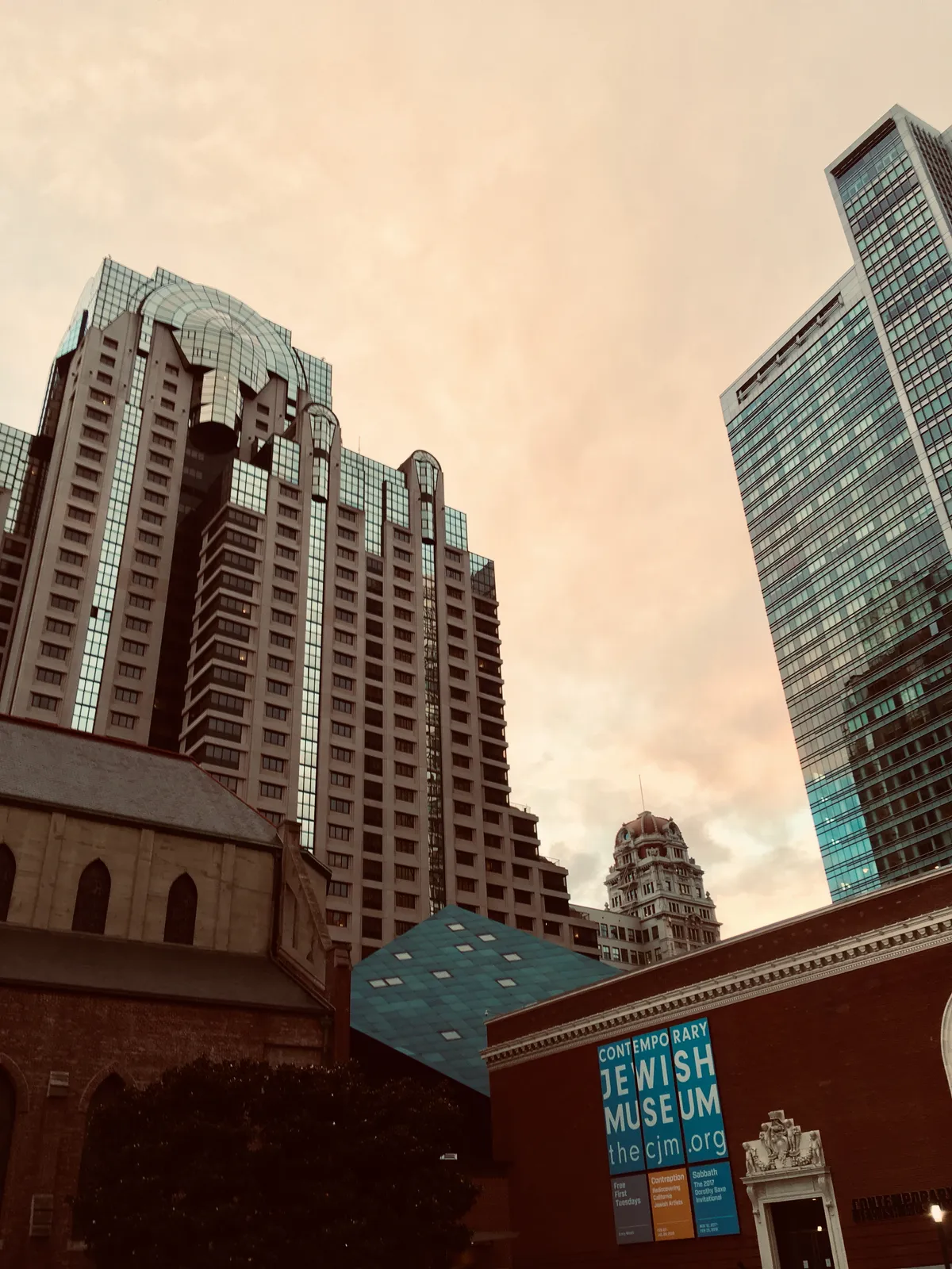 Contemporary Jewish Museum with blue geometric extension surrounded by tall downtown San Francisco buildings during sunset