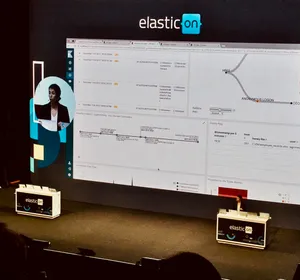 ElasticON conference presentation showing security analytics dashboard on large screen with Elastic branded boxes on stage in San Francisco