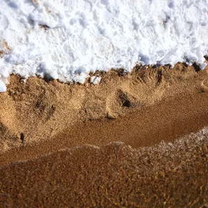 Close-up view of white foamy water washing over textured golden sand at Lake Tahoe beach in Bijou, California