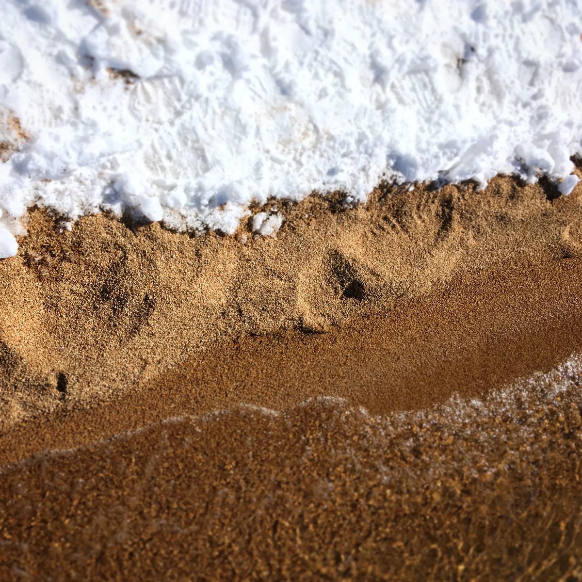Close-up view of white foamy water washing over textured golden sand at Lake Tahoe beach in Bijou, California