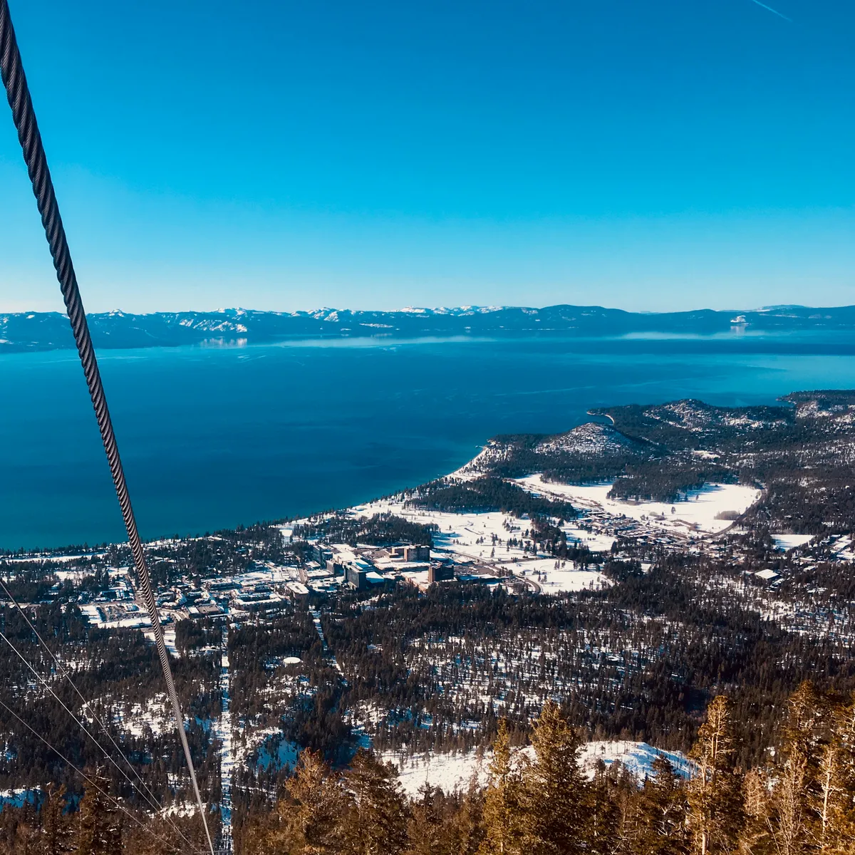 Aerial view from gondola overlooking Lake Tahoe with snow-covered mountains, forested valleys, and developed areas visible below in Kingsbury