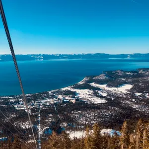 Aerial view from gondola overlooking Lake Tahoe with snow-covered mountains, forested valleys, and developed areas visible below in Kingsbury