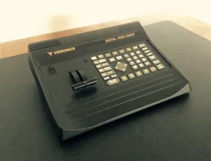 Black Videonics Digital Video Mixer control panel with multiple white buttons, joystick, and two black knobs on dark surface in Waidach, Austria