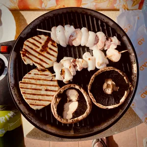 Seafood skewers and large mushrooms cooking on ridged grill pan at camping site in Bibbona, Italy