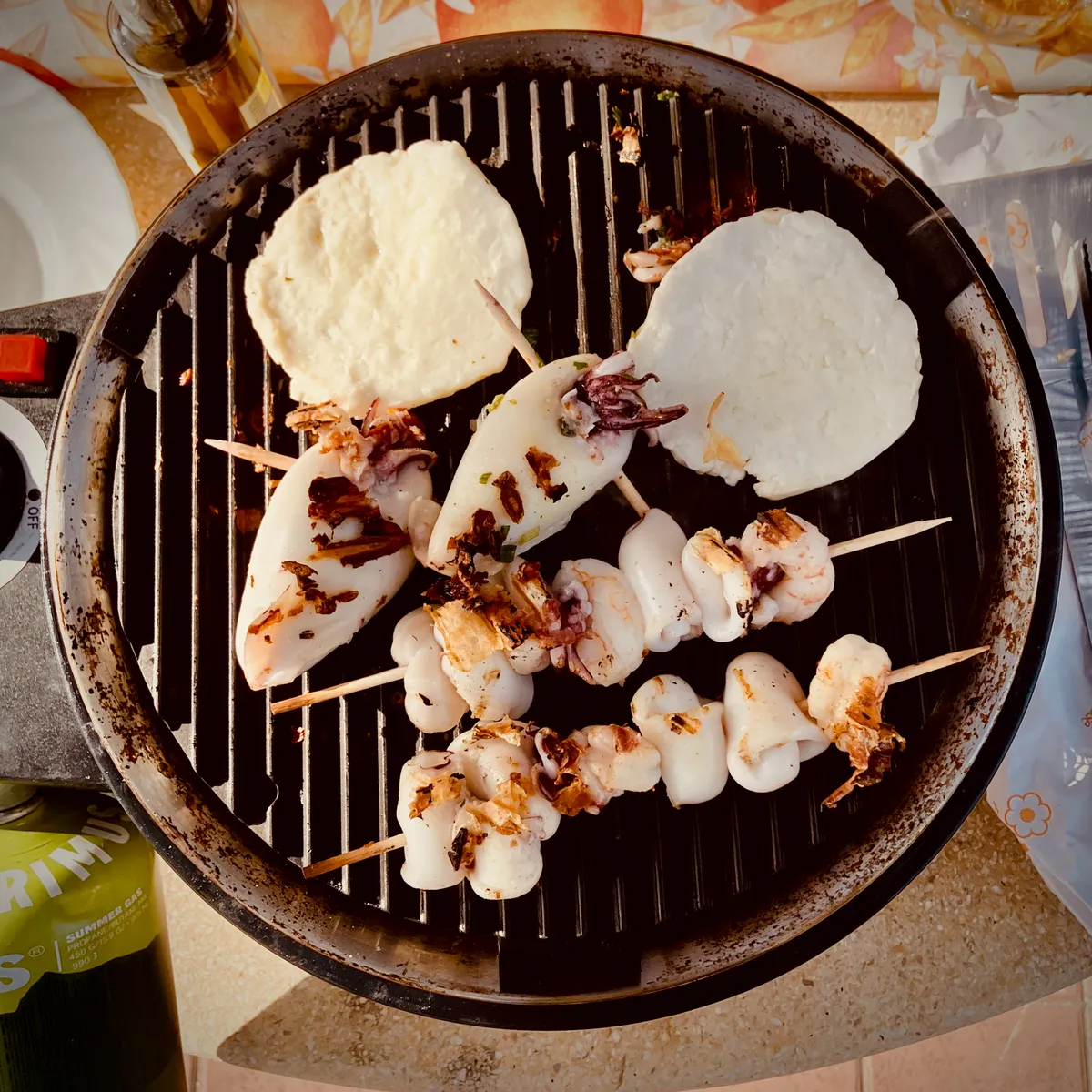 Seafood skewers with calamari and shrimp cooking on round charcoal grill with flatbread at camping site in Bibbona, Italy
