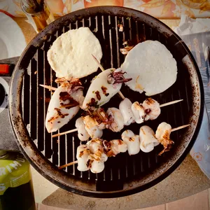 Seafood skewers with calamari and shrimp cooking on round charcoal grill with flatbread at camping site in Bibbona, Italy