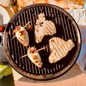 Large fish fillets and bacon-wrapped seafood skewers cooking on ridged cast iron grill pan at Bibbona camping site, Italy