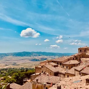 Medieval hilltop town of Volterra with red tile roofs overlooking rolling Tuscan countryside and distant mountains under blue sky