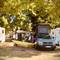 Yellow hammock stretched between trees next to white VW T4 camper van at campground in Pieve, Italy with other RVs visible