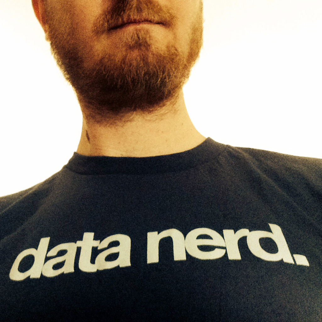 Close-up photo of a black t-shirt with white text reading 'data nerd', showing part of the wearer's bearded chin. The image appears to have a warm, sepia-toned filter.